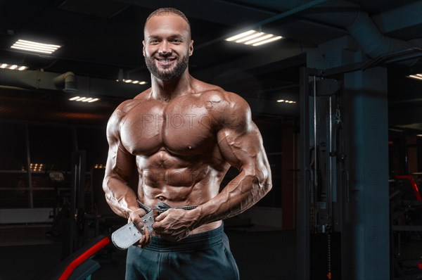 Muscular man poses in the gym with an athletic belt. Sports