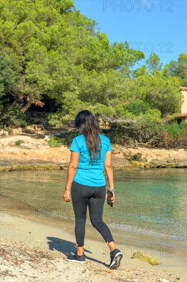 Latina woman in sportswear walking and listening to music with her smart phone on the beach