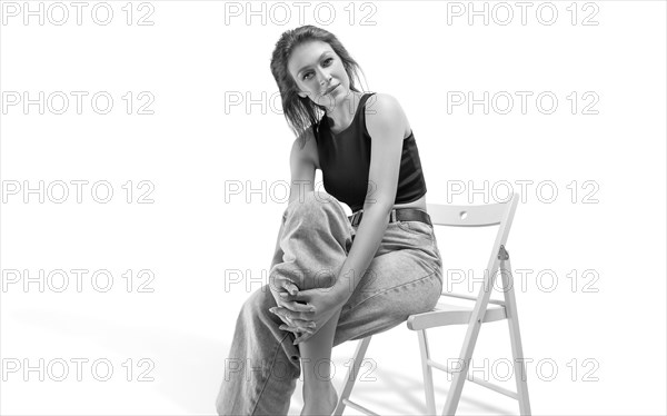 Beautiful girl posing on a white background sitting on a chair in a black bodysuit and jeans. Underwear advertising concept.