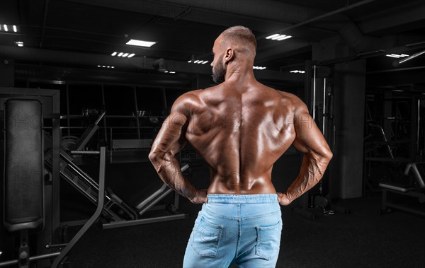 Muscular man in jeans poses in the gym. Sports