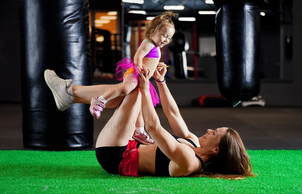 Charming sports mom plays in the gym with her little daughter.