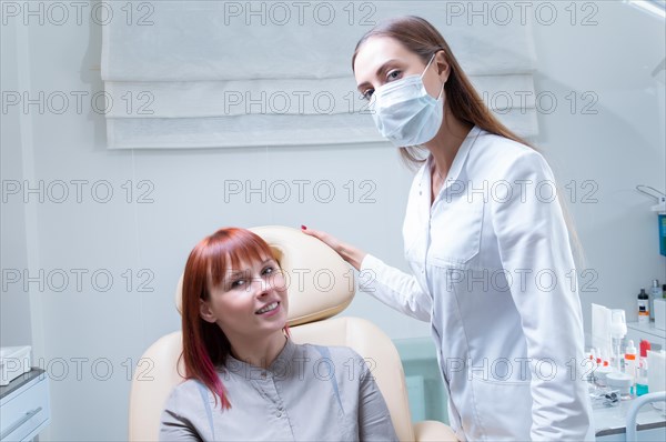 Beautician consults a woman in a beauty salon. The patient sits in a cosmetic chair and smiles at the specialist.