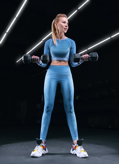 Charming sportswoman posing in the gym with dumbbells. The concept of bodybuilding