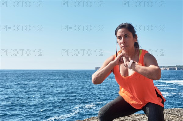 Woman in active wear doing squats by the ocean under a clear blue sky