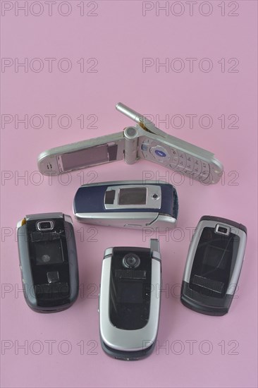 A birds-eye view of classic flip phones on a plain pink background