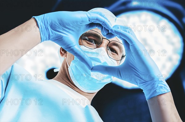 Portrait of a doctor on the background of surgical lamps. He made a heart out of his hands. Medicine concept.