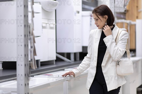 Beautiful young woman in a white jacket chooses plumbing supplies in a hardware store