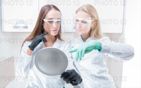 Two beauticians pose in a medical salon with a mirror in their hands. Rejuvenation concept.