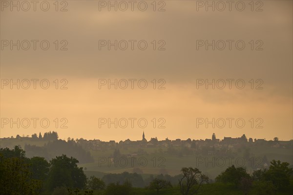 Silhouette of a village on a hill under an orange-coloured sky at sunrise