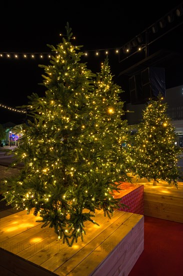 Christmas tree in pot with red decorations and lights outdoors near grey loft building