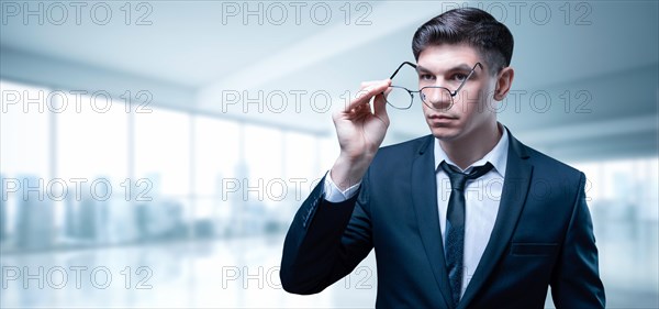 Portrait of a businessman in a skyscraper office. He fix his glasses with a serious expression on his face.