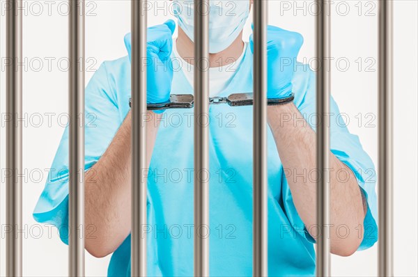 Doctor in handcuffs is standing behind a prison cell. The concept of corruption in medicine.
