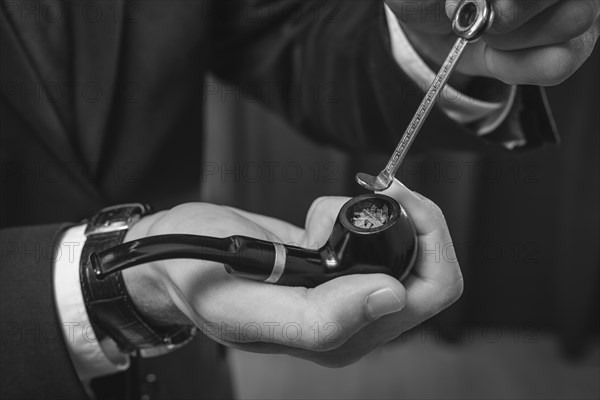 Image of male hands holding a smoking pipe and tamper. Tobacco smoking concept.