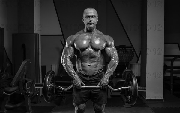 Professional weightlifter posing in the gym with a barbell in his hands. Classic bodybuilding.