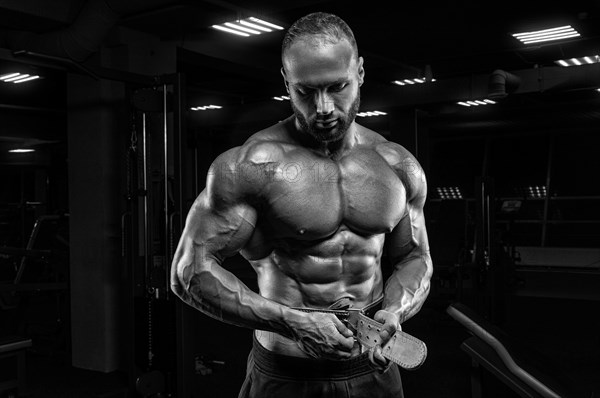 The athlete poses in the gym with an athletic belt. Fitness