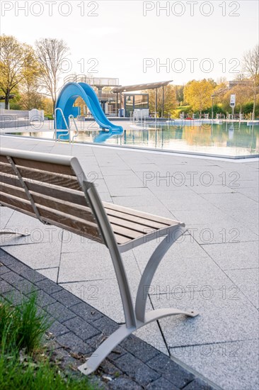 Lonely bench next to an empty swimming pool near a slide and clear water pool