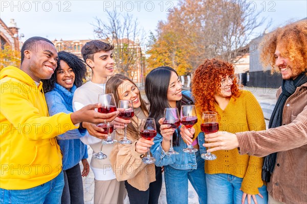 Multi-ethnic friends smiling and toasting with red wine in the street