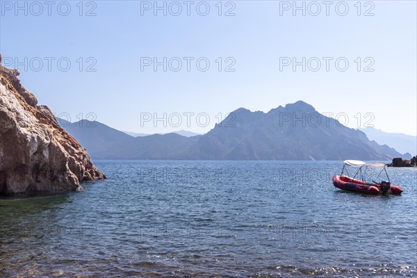A red boat floats peacefully on clear blue water near jagged cliffs under a vast sky