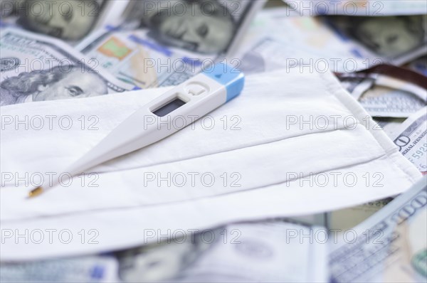 Medical mask and a thermometer lie on one hundred dollar bills. The concept of an epidemic