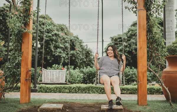 Portrait of smiling girl sitting on a swing in a garden. Happy young woman sitting on a swing in a beautiful garden