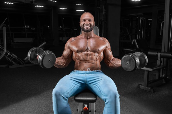 The athlete is doing the exercise in the gym. Lifting dumbbells while sitting on a bench. Fitness