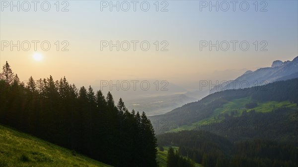 Sunrise over a misty mountain landscape with forest in the foreground