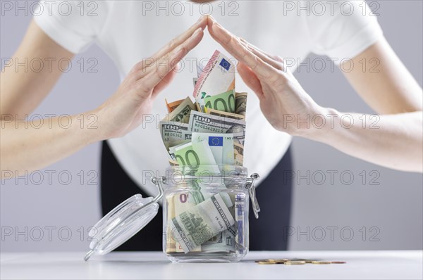 Woman imitates a roof from her hands over a piggy bank full of cash notes. The concept of family thrift in a crisis.