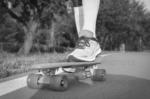 Images of a leg standing on a skateboard. Sunny evening in the park. Skateboarding concept.