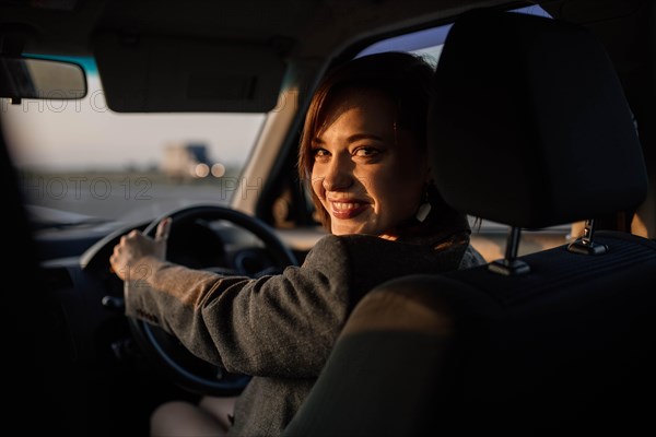 Young beautiful smiling female taxi driver in a jacket greets passengers in a friendly manner