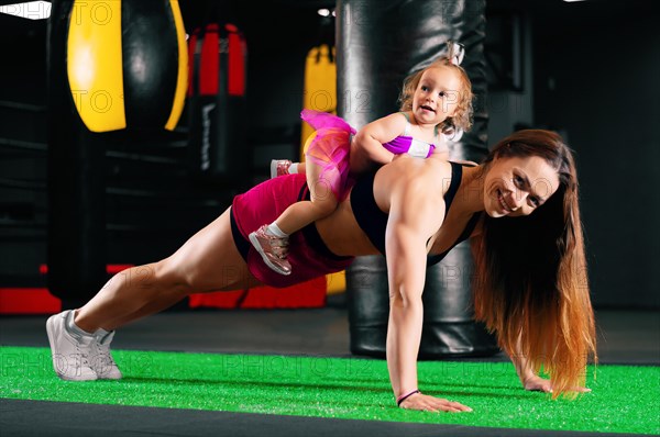 Charming young mother is wringing out with her daughter. The girl is sitting on her mother's back. Joint trainings