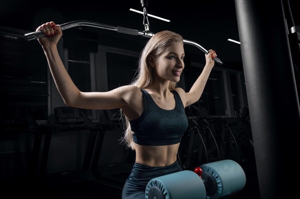 Charming blonde does exercises for the back in the gym. Neck pull for the head. The concept of sports