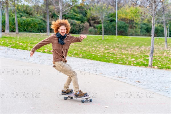 Redheaded curly hair Young man skating in a park in autumn