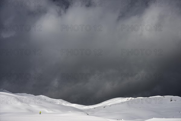 Ski tourer on a vast plateau with snow-covered mountains in the background and dramatic sky