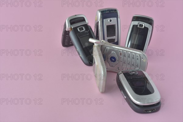 Two vintage flip phones open and standing among other models on a pink background