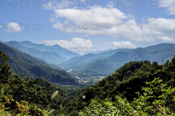 Scenic view of a green valley surrounded by lush mountains under a cloudy sky in Nagari Gaon