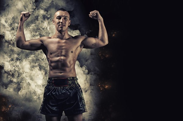 Portrait of a boxer of mixed martial arts standing against the backdrop of smoke and fire and celebrating a victory. The concept of sports