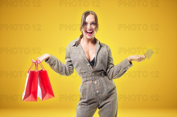 Beautiful tall woman with red packages in her hands. Pre-holiday shopping concept. Yellow background.