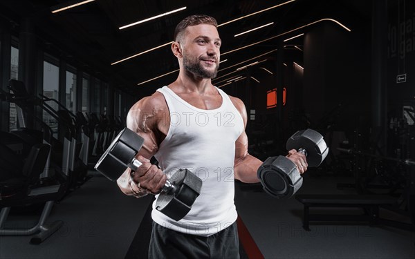 Image of a muscular guy in a white jersey with sports equipment. Gym. Fitness concept