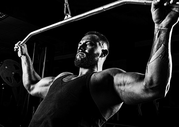 Professional athlete performs an exercise in the gym. Pulls the bar to his chest. Exercise for development of back muscles