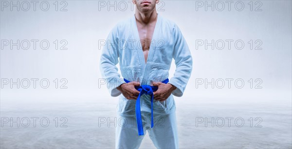 Athlete in a kimono with a blue belt stands on a light background. The concept of karate and judo.