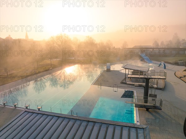 The sun's rays penetrate the fog over a swimming pool with slides