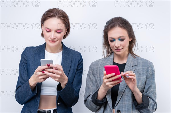 Portrait of two women each looking at her phone. The concept of social problems. Deficit of communication due to social media.