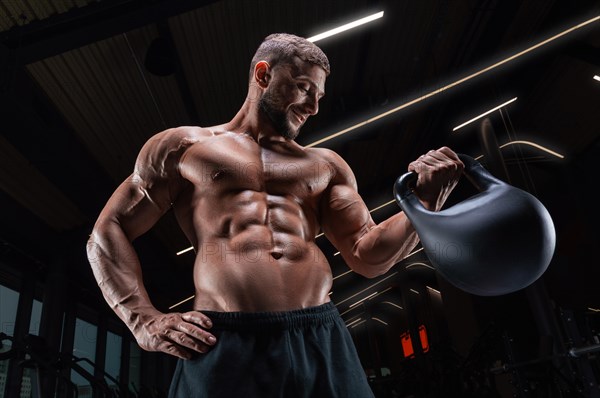Muscular man posing in the gym with a kettlebell. Fitness concept.