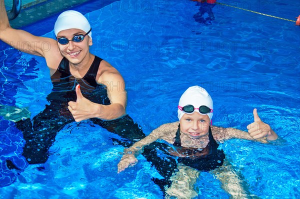 Charming coach with his student swimming in the pool and smiling