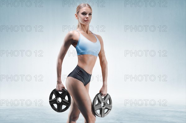Beautiful girl posing with weight plates in her hands on a blue background. The concept of sports