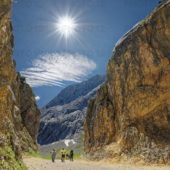 A group of hikers between imposing rock faces under a bright blue sky with the sun above