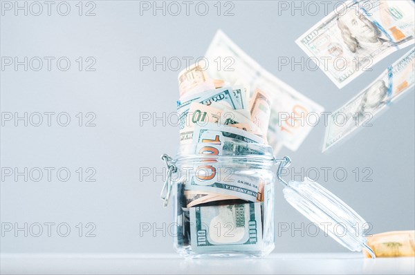 Glass piggy bank full of money. Banknotes are strewed from above. The concept of squandering.