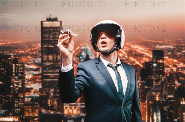 Portrait of a man in a suit and helmet. He launches a paper airplane from the roof of a skyscraper. Business concept.