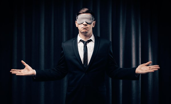 Portrait of a man in a mask for sleeping. He stands against the backdrop of a curtain. The concept of blind dates