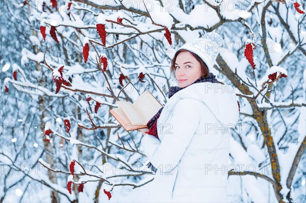 Portrait of a charming girl who reads a book in the winter forest. Concept of Christmas